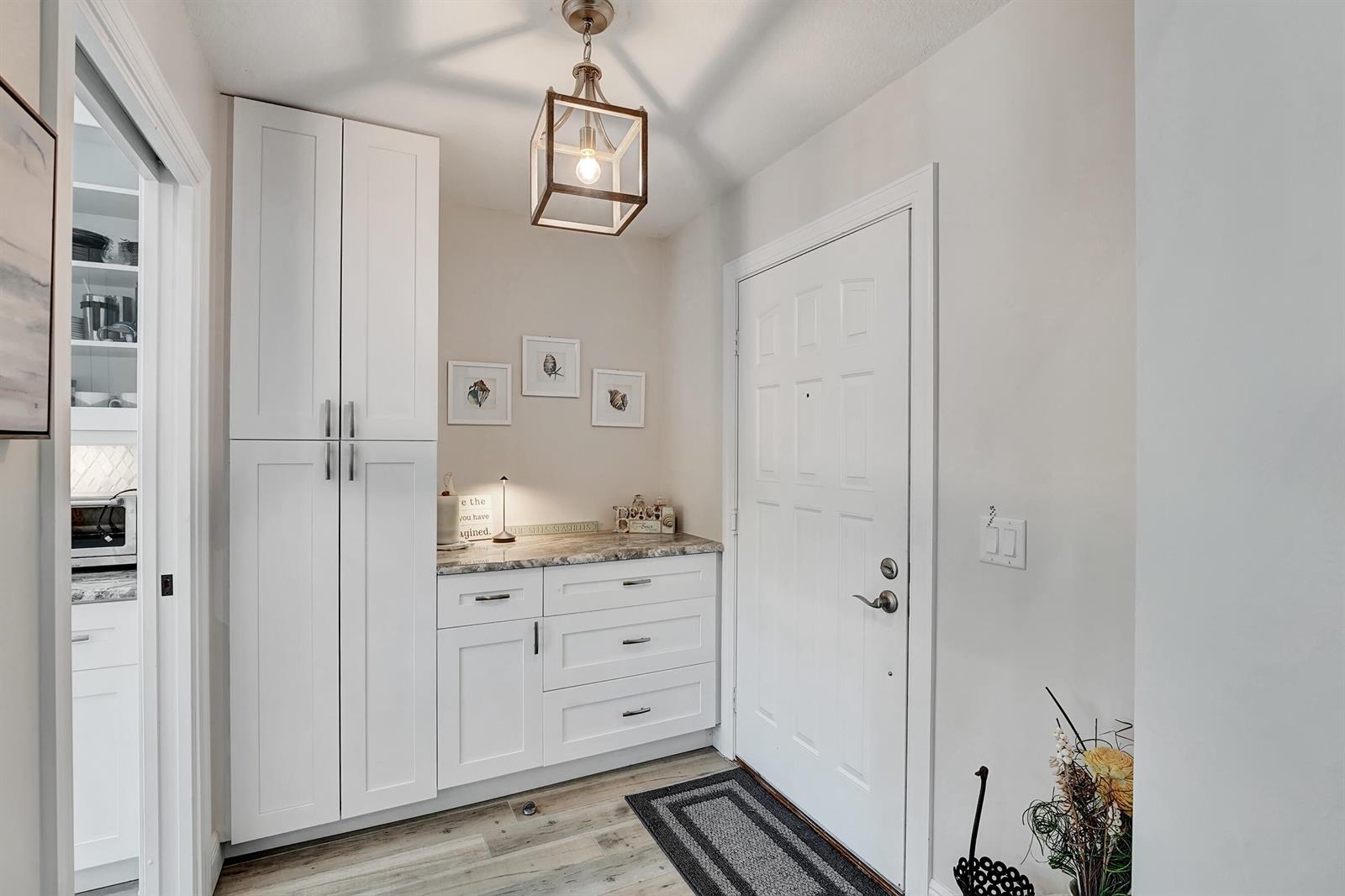 A white entryway features a tall storage cabinet, a countertop, and a hanging lantern light — 118 Ridge Road, Jupiter FL 33477, JUPITER, FL