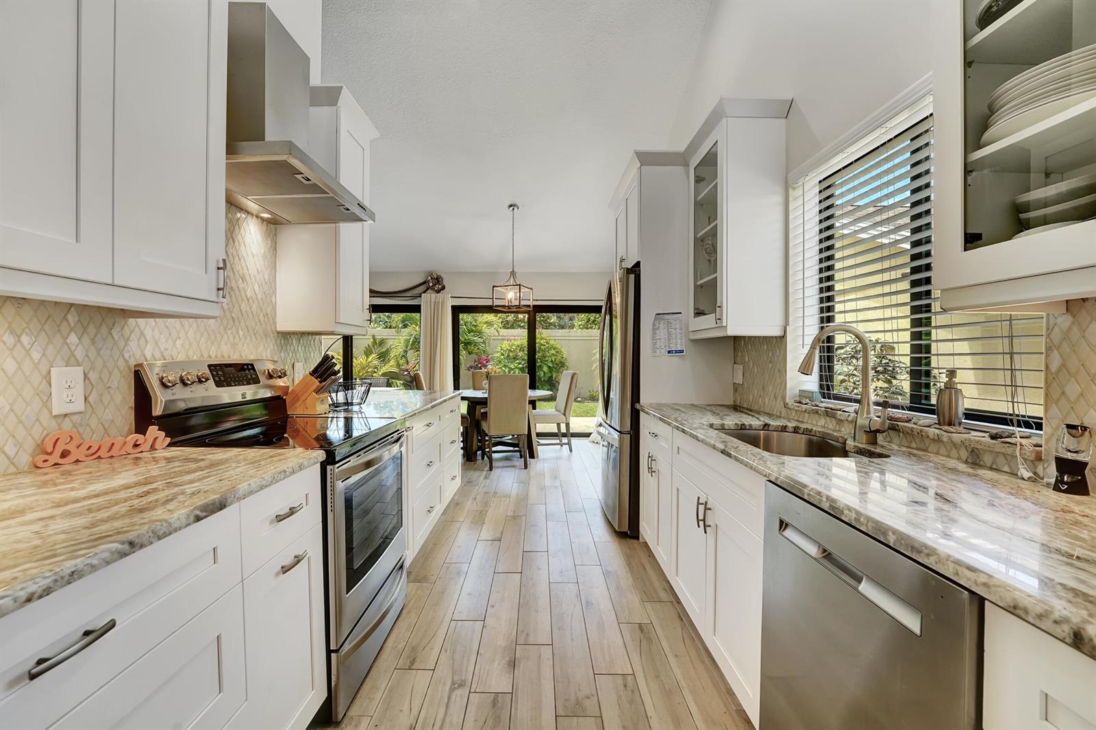 A galley kitchen features white cabinets, granite countertops, stainless steel appliances, and wood-look tile flooring — 118 Ridge Road, Jupiter FL 33477, JUPITER, FL