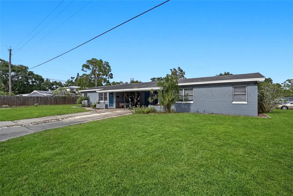 A single-story gray house with a carport sits on a large, grassy lawn — 7301 8TH STREET N, ST PETERSBURG, FL