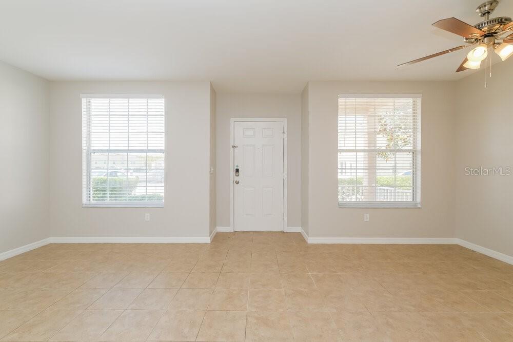 An empty room with beige tile flooring, two windows with blinds, and a front door — 5048 CACTUS NEEDLE LANE, WESLEY CHAPEL, FL