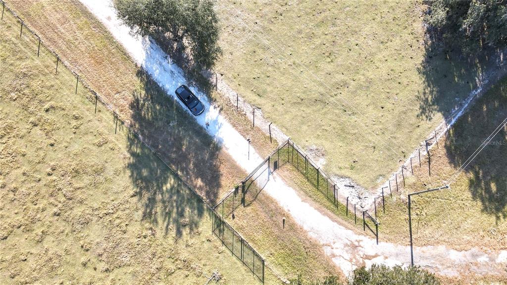 An aerial view shows a dark car parked on a gravel driveway near a fenced gate — 7223 SW 55TH STREET, BUSHNELL, FL
