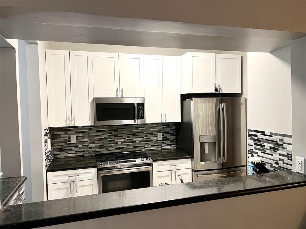 A kitchen features white cabinets, stainless steel appliances, a dark countertop, and a mosaic backsplash — 7085 Nova Drive # 226, Davie FL 33317, DAVIE, FL