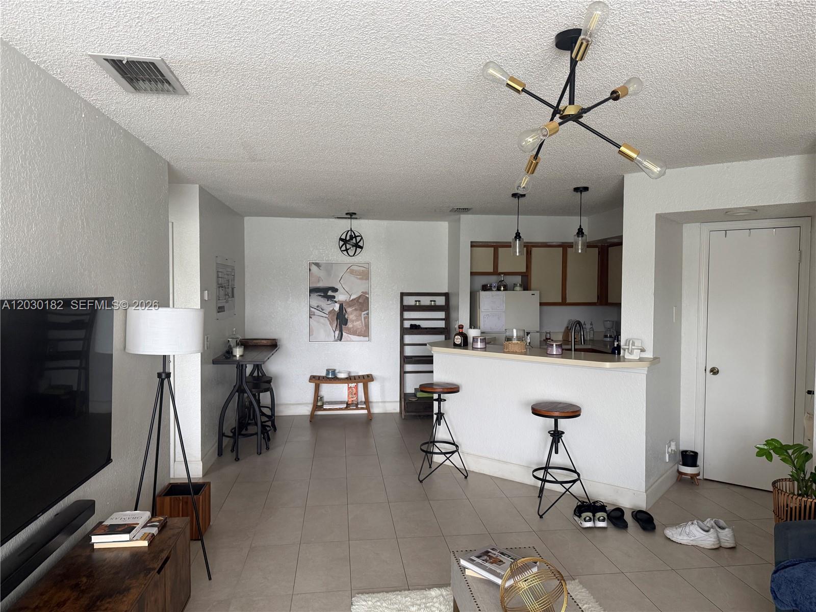 An empty room features white walls, tile flooring, a modern chandelier, and a laundry closet — 3330 N Pinewalk Dr N # 1623, Margate FL 33063, MARGATE, FL