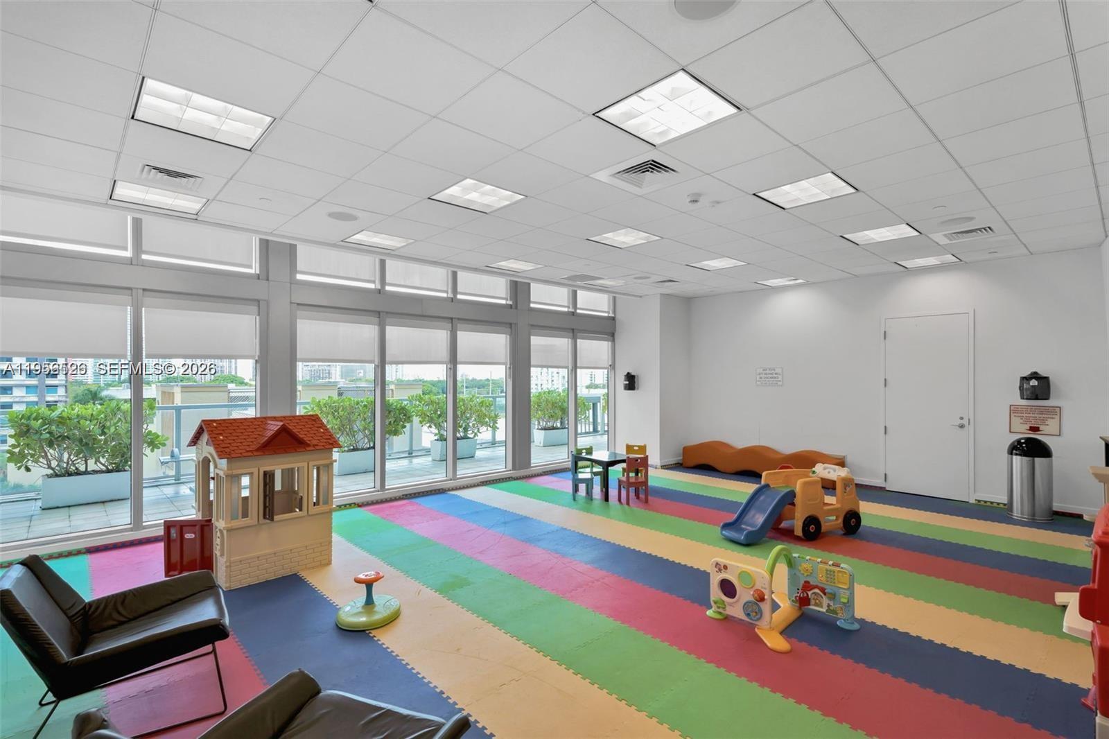 A brightly lit indoor children's playroom features colorful floor mats, toys, and floor-to-ceiling windows — 1111 SW 1st Ave, Miami FL 33130, MIAMI, FL