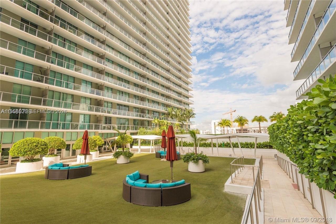 An outdoor terrace features artificial turf, circular seating with blue cushions, and red umbrellas — 1111 SW 1st Ave, Miami FL 33130, MIAMI, FL