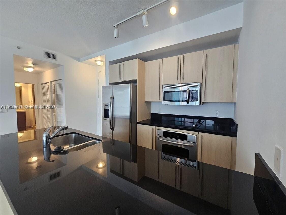 A modern kitchen features light wood cabinets, black countertops, and stainless steel appliances — 1111 SW 1st Ave, Miami FL 33130, MIAMI, FL