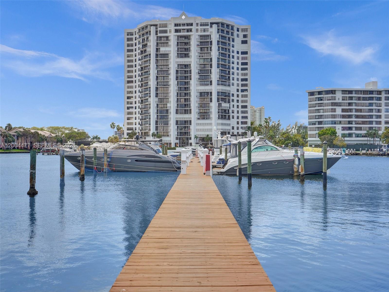 A wooden dock extends into a waterway between two yachts with a high-rise building behind — 2667 S Parkview Dr, Hallandale Beach FL 33009, HALLANDALE BEACH, FL