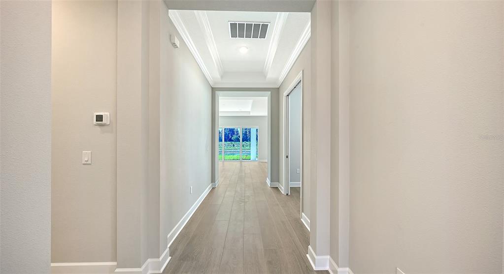 A hallway with light wood-look flooring leads toward a bright room with glass sliding doors — 10248 SILENT NIGHT LANE, SARASOTA, FL