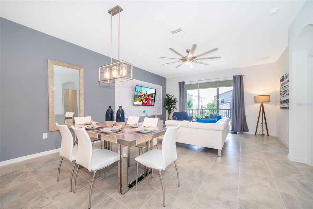 A dining area with a modern chandelier and table sits before an open living room — 8861 CABOT CLIFFS DRIVE UNIT 104, DAVENPORT, FL