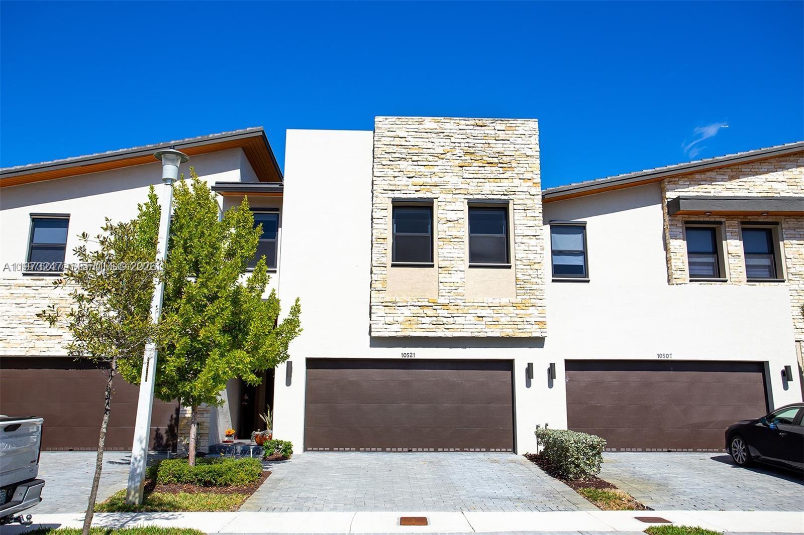 A two-story townhouse exterior features a stone facade, white stucco walls, and two garage doors — 10521 NW 81st Ter, Doral FL 33178, DORAL, FL
