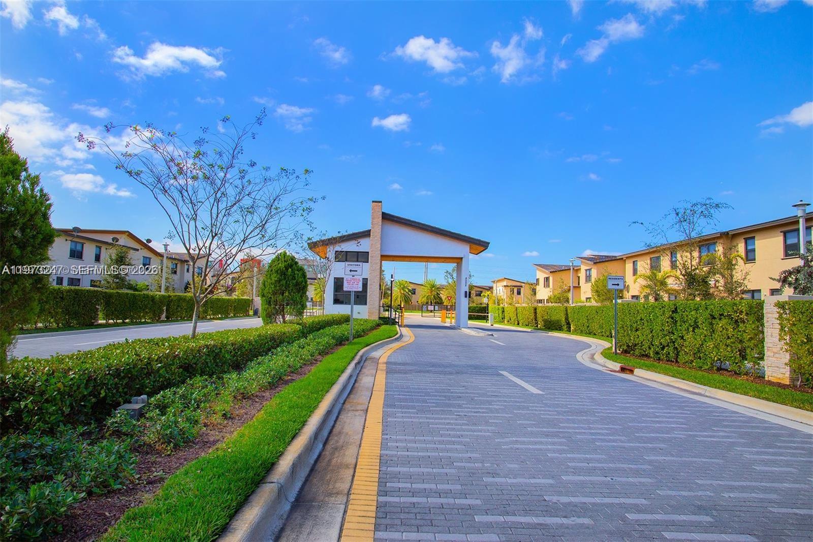 A paved driveway leads to a gated community entrance with a modern guardhouse structure — 10521 NW 81st Ter, Doral FL 33178, DORAL, FL