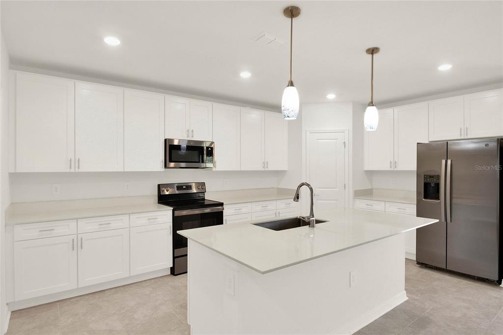 A modern kitchen features white cabinetry, stainless steel appliances, and a central island with seating — 271 INMAN BOULEVARD, WINTER HAVEN, FL