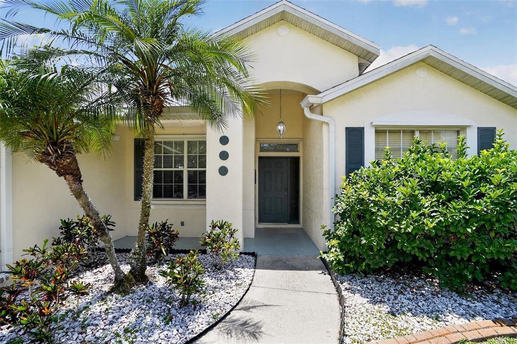 A single-story house exterior features a palm tree, a concrete walkway, and a dark door — 11226 PRIMROSE CIRCLE, BRADENTON, FL