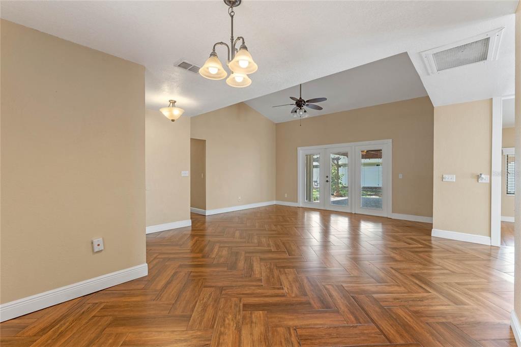 An empty room features herringbone wood-look flooring, a vaulted ceiling, and glass patio doors — 521 LAKESHORE CIRCLE, LAKE MARY, FL