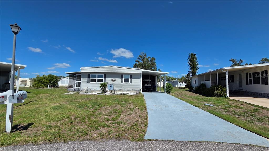 A single-story manufactured home with a light gray exterior, a carport, and a front lawn — 6881 HOLO COURT, NORTH PORT, FL