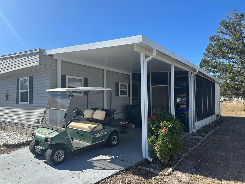 A green golf cart is parked under a carport attached to a light-gray mobile home — 6881 HOLO COURT, NORTH PORT, FL