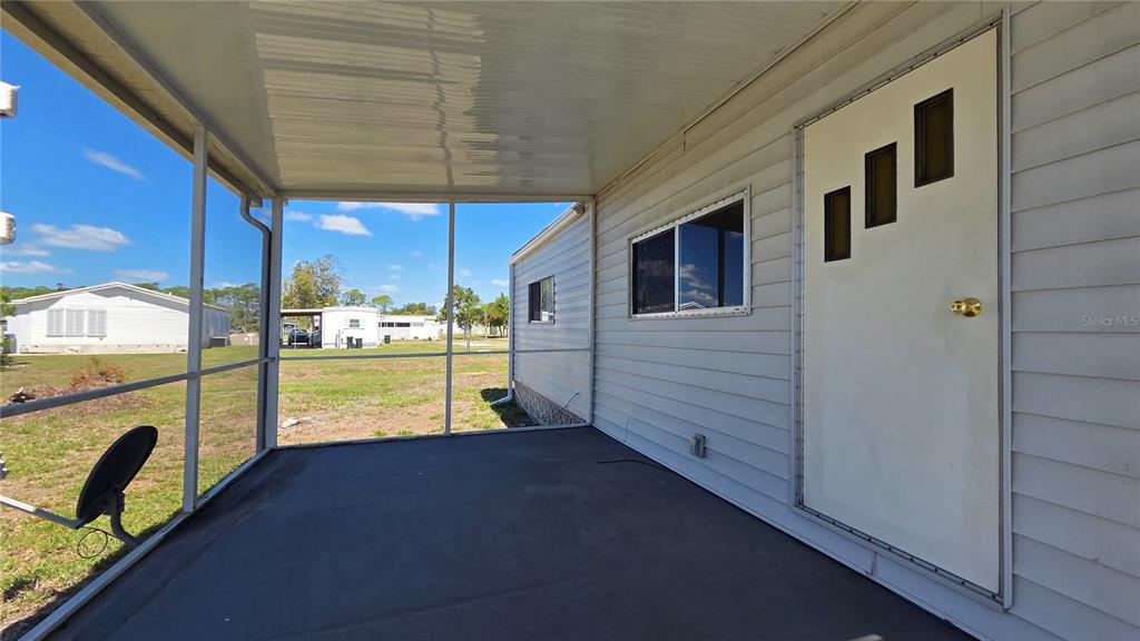 A covered, screened-in porch with a white door and siding overlooks a grassy yard — 6881 HOLO COURT, NORTH PORT, FL