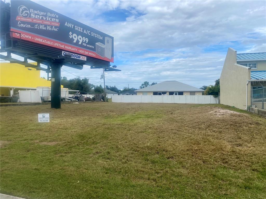 A vacant, grassy lot sits beneath a large billboard next to a residential building — 3782 N ACCESS ROAD, ENGLEWOOD, FL