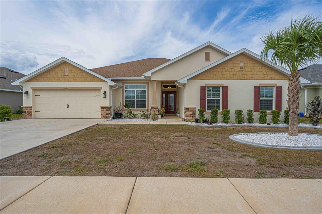 A single-story suburban house with a tan stucco exterior, shingled roof, and a palm tree — 5035 SW 91ST PLACE, OCALA, FL