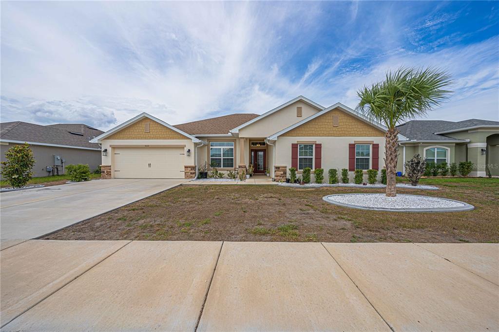 A single-story suburban house features a two-car garage, tan stucco siding, and a palm tree — 5035 SW 91ST PLACE, OCALA, FL