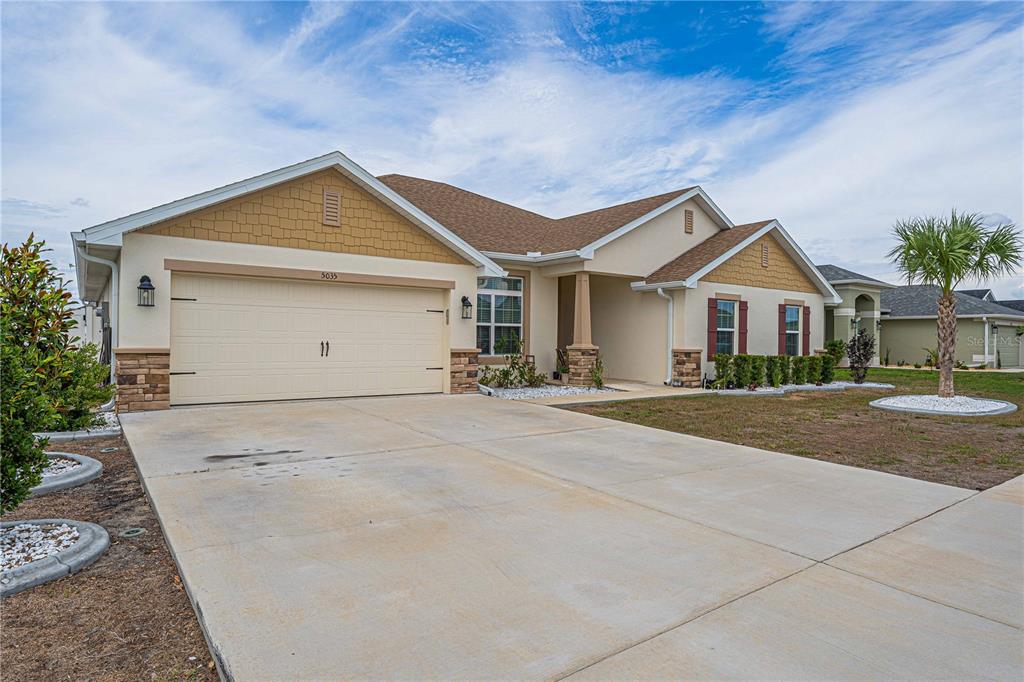 A single-story suburban house features a two-car garage, tan stucco siding, and stone accents — 5035 SW 91ST PLACE, OCALA, FL