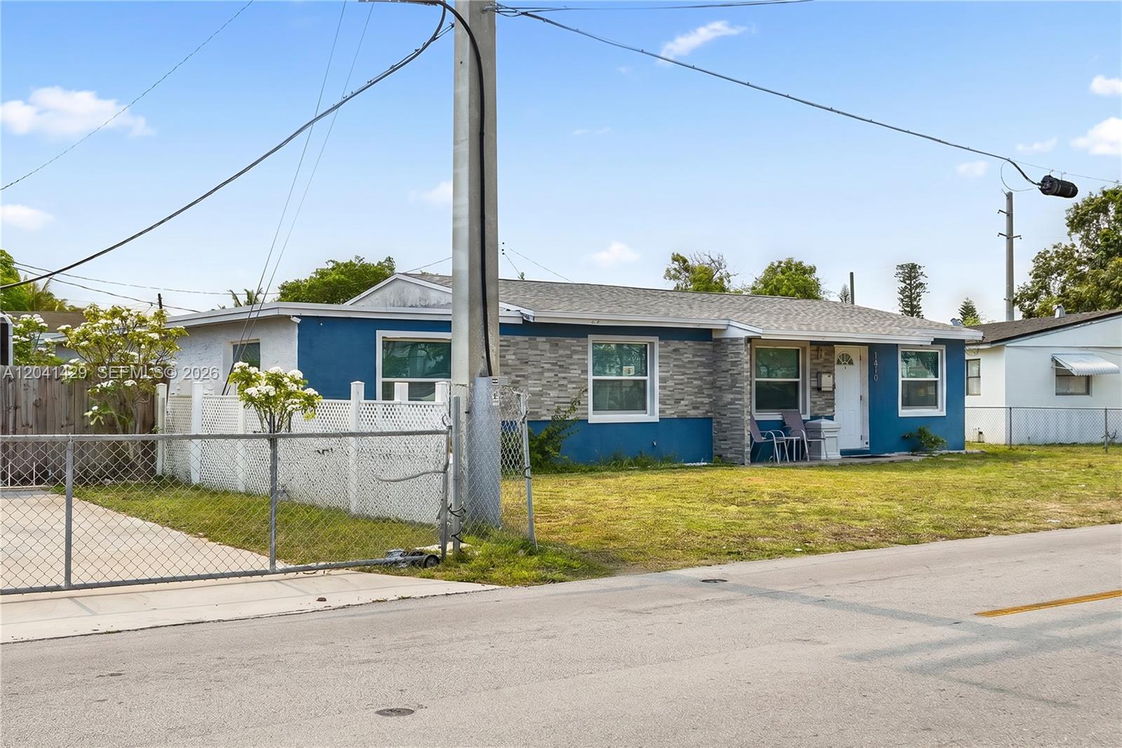 A blue single-story house features a stone facade, white trim, and a chain-link fence — 1610 S 22nd Ave, Hollywood FL 33020, HOLLYWOOD, FL