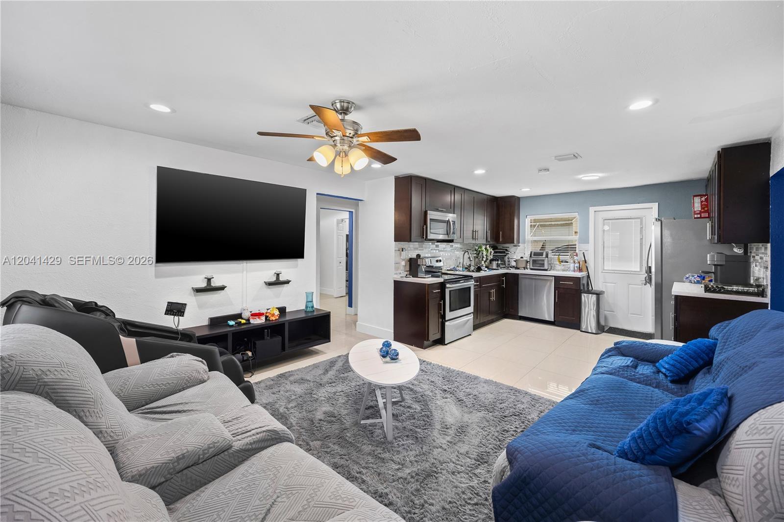 A living room with a large television and a kitchen with dark wood cabinets — 1610 S 22nd Ave, Hollywood FL 33020, HOLLYWOOD, FL