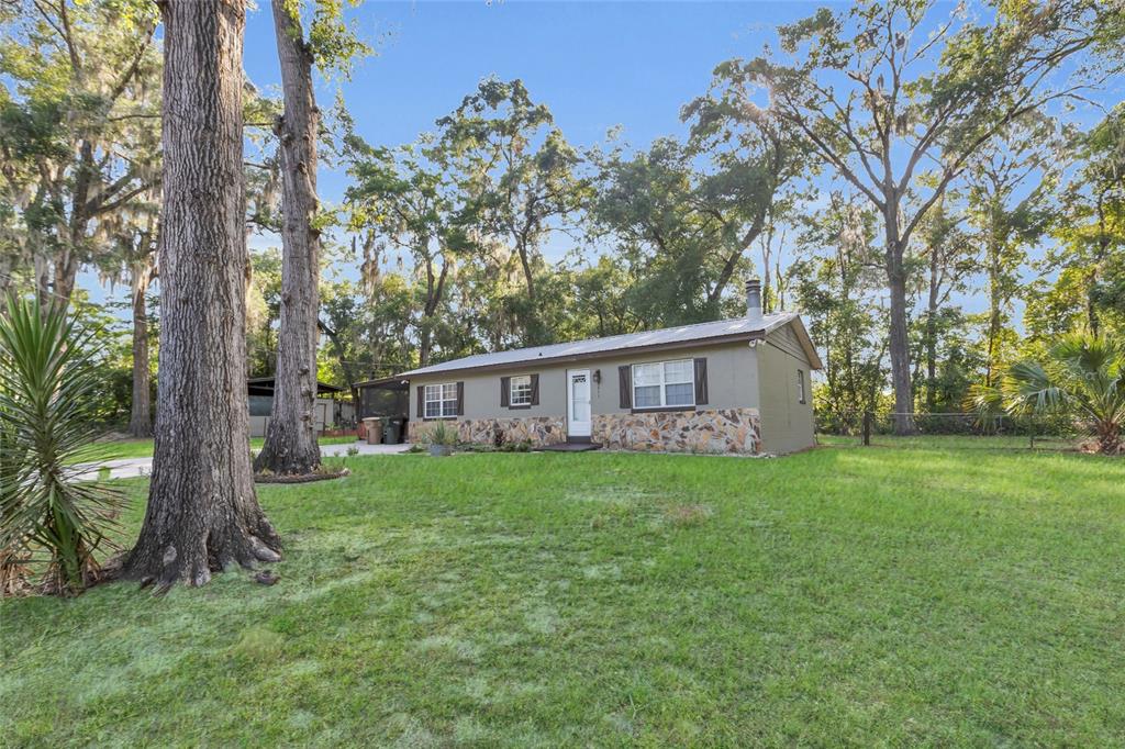 A single-story house with stone siding and a metal roof sits on a grassy lot — 2015 NE 12TH AVENUE, OCALA, FL