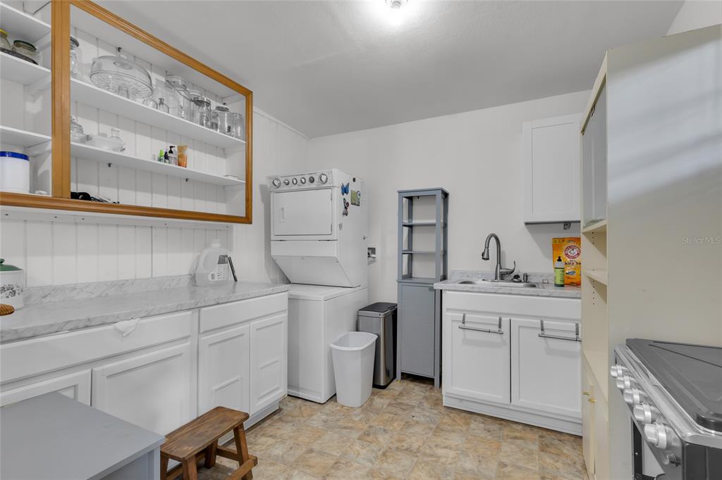 A laundry room features white cabinetry, a stacked washer and dryer, and a utility sink — 2015 NE 12TH AVENUE, OCALA, FL