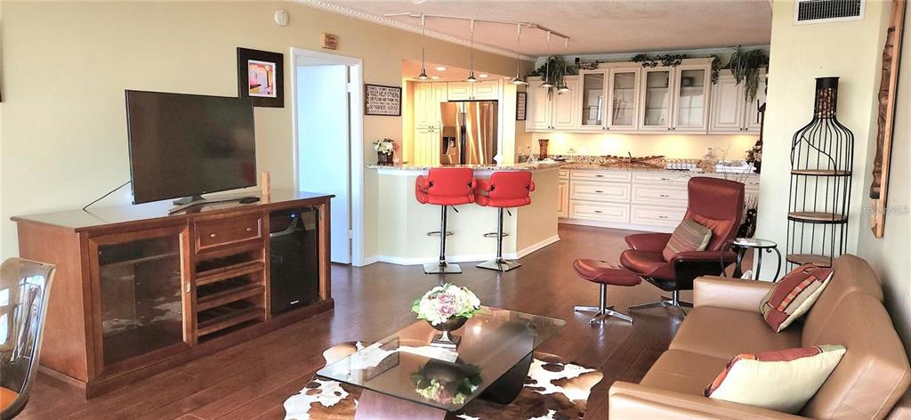 A living room with a television console, leather sofa, and an open kitchen with stools — 7100 SUNSHINE SKYWAY LANE S UNIT 906, ST PETERSBURG, FL
