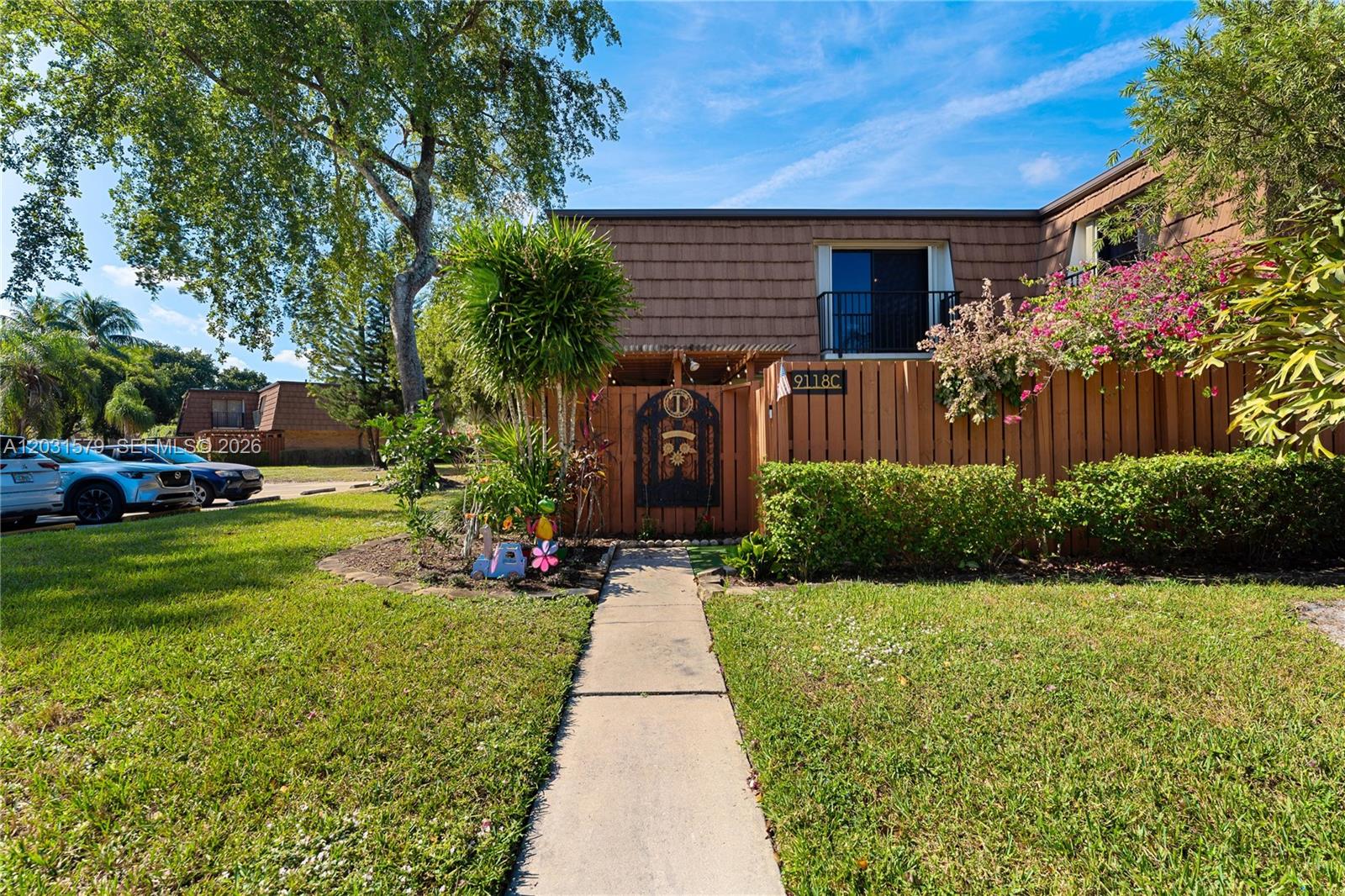A concrete walkway leads to a fenced courtyard entrance of a two-story brown townhouse — 9118c 20th ct, Davie FL 33324, DAVIE, FL