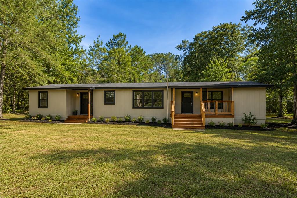 A single-story house with tan siding, black window frames, and two wooden front porch entrances — 7056 VANCE STREET, BROOKSVILLE, FL