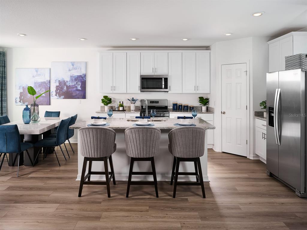 A modern kitchen features white cabinets, stainless steel appliances, a granite island, and gray barstools — 857 SILVERADO TRAIL DRIVE, LAKE HAMILTON, FL