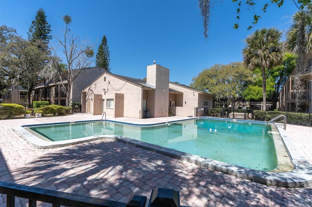 An outdoor swimming pool with a brick paver deck sits in front of a building — 7606 ABBEY LANE UNIT 208, TAMPA, FL