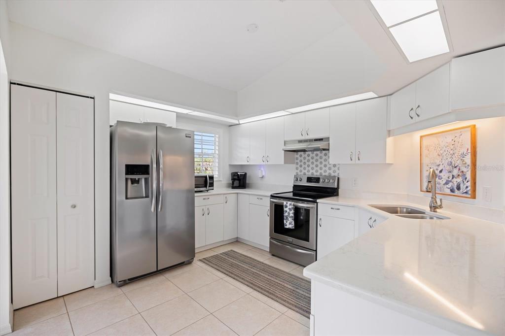 A bright kitchen features white cabinets, stainless steel appliances, and light-colored countertops — 801 MONTROSE DRIVE UNIT 202, VENICE, FL