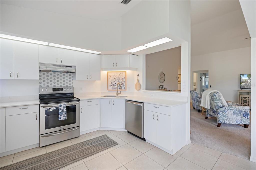 A white kitchen features stainless steel appliances, a tiled backsplash, and an adjacent living area — 801 MONTROSE DRIVE UNIT 202, VENICE, FL