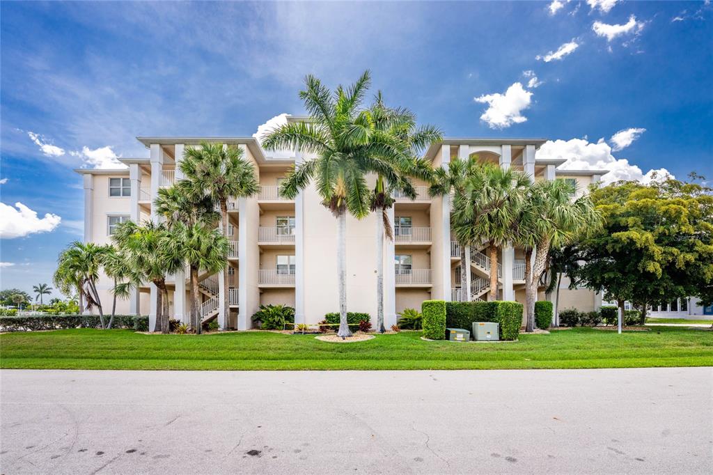 A multi-story residential building with balconies and palm trees sits behind a grassy lawn — 268 LEWIS CIRCLE UNIT 143, PUNTA GORDA, FL