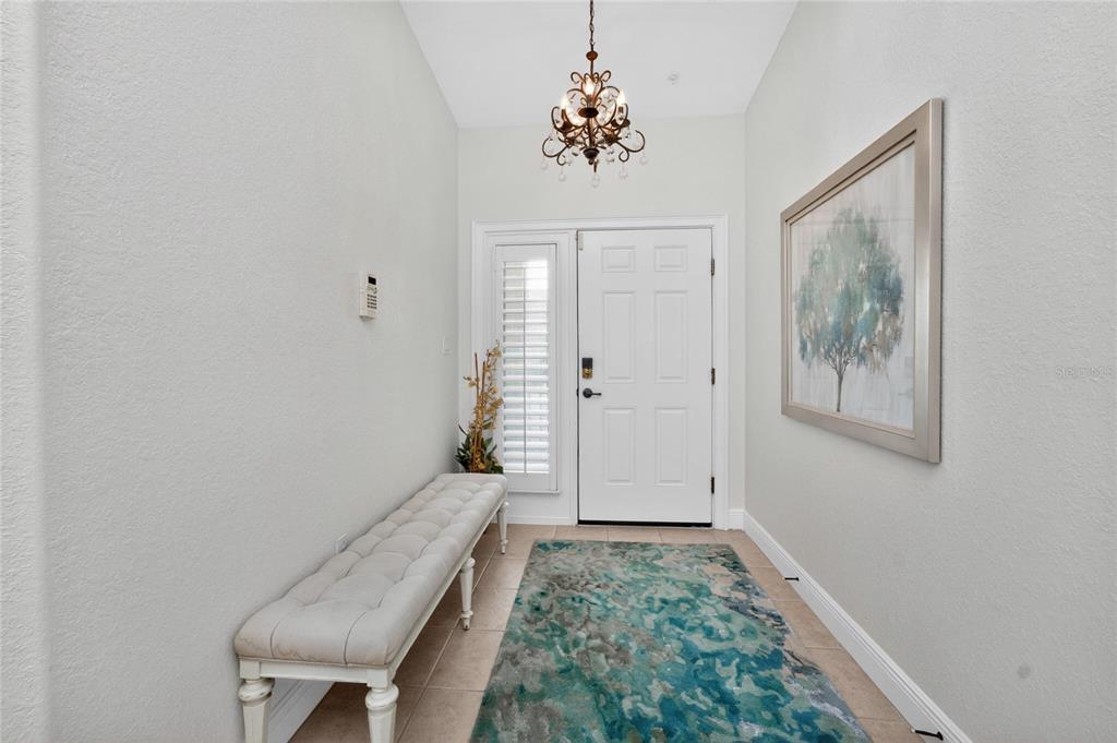 A bright entryway features a tufted bench, a patterned area rug, and a hanging chandelier — 268 LEWIS CIRCLE UNIT 143, PUNTA GORDA, FL