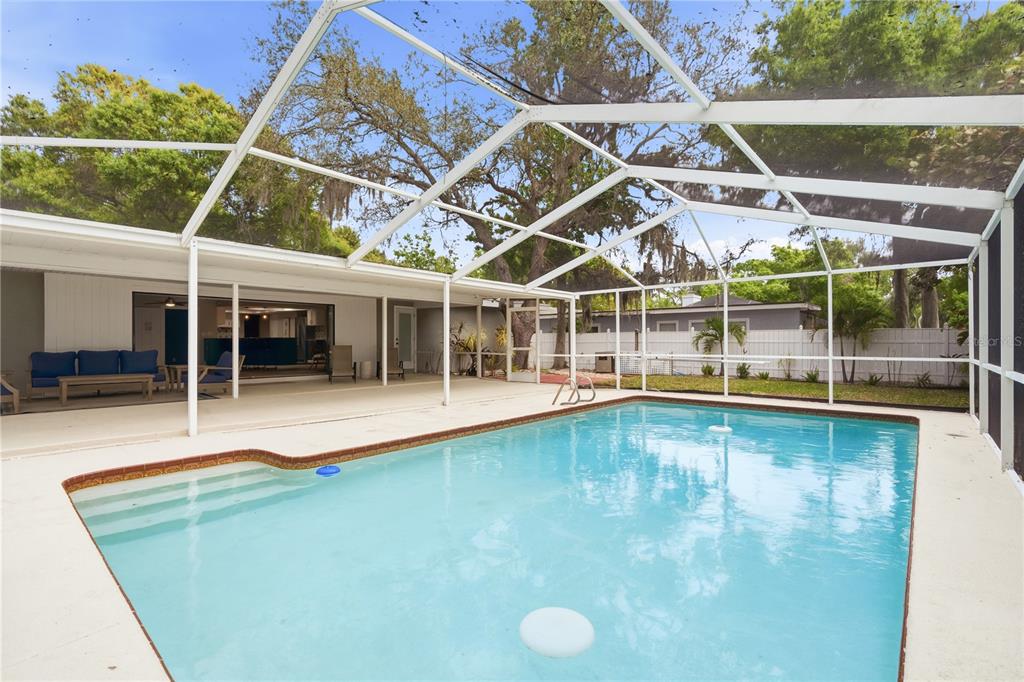 A swimming pool with a screened-in enclosure sits on a patio outside a house — 13012 96TH AVENUE, SEMINOLE, FL