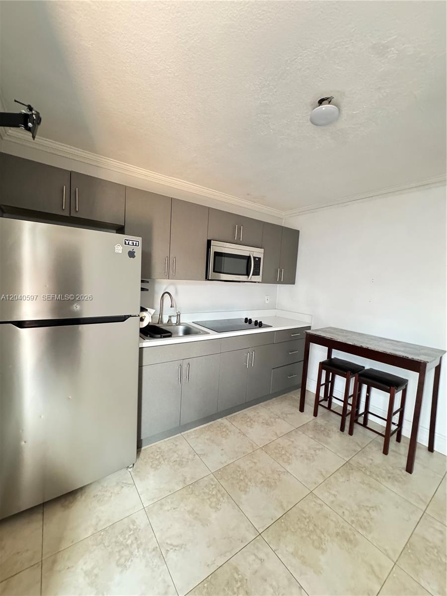 A small kitchen features gray cabinets, stainless steel appliances, and a high-top dining table — 11340 SW 41st Ter, Miami FL 33165, MIAMI, FL