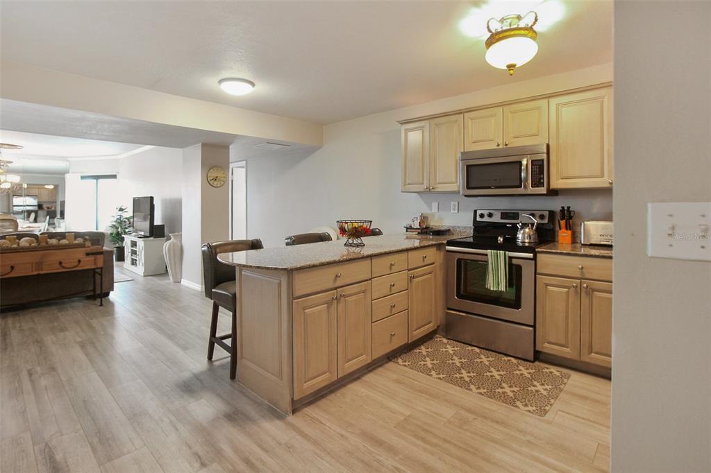 A kitchen with light wood cabinets, granite countertops, and stainless steel appliances opens to a living area — 1050 LONGBOAT CLUB ROAD UNIT 702, LONGBOAT KEY, FL