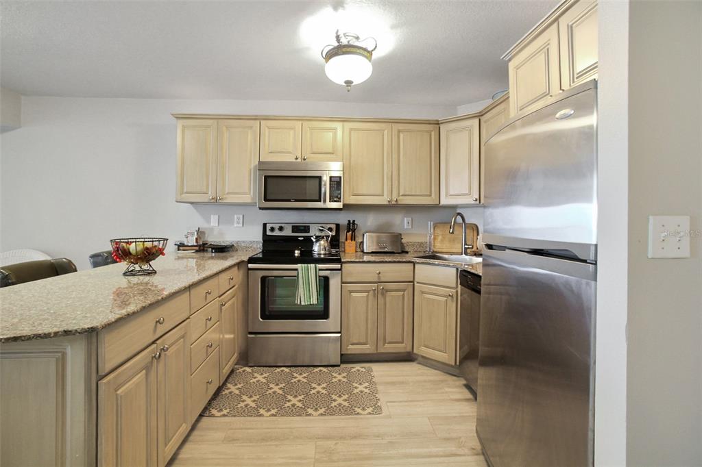 A kitchen features light wood cabinets, granite countertops, stainless steel appliances, and wood-look flooring — 1050 LONGBOAT CLUB ROAD UNIT 702, LONGBOAT KEY, FL