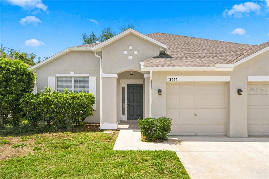 A single-story house with a beige stucco exterior, a gray front door, and a garage — 13444 HAVERHILL DRIVE, SPRING HILL, FL