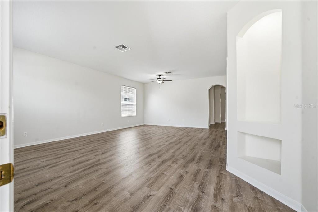 An empty living room features white walls, wood-look flooring, a ceiling fan, and wall niches — 13444 HAVERHILL DRIVE, SPRING HILL, FL