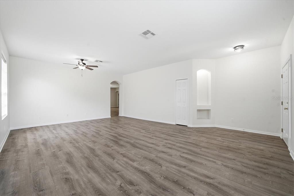 A spacious, empty living room with white walls, gray wood-look flooring, and a ceiling fan — 13444 HAVERHILL DRIVE, SPRING HILL, FL