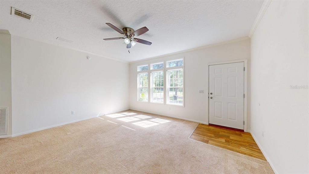 An empty living room features beige carpet, white walls, a ceiling fan, and a front door — 2930 PALMETTO STREET, BUNNELL, FL