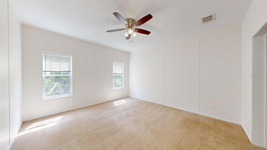 An empty bedroom features beige carpet, white walls, two windows, and a ceiling fan — 2930 PALMETTO STREET, BUNNELL, FL