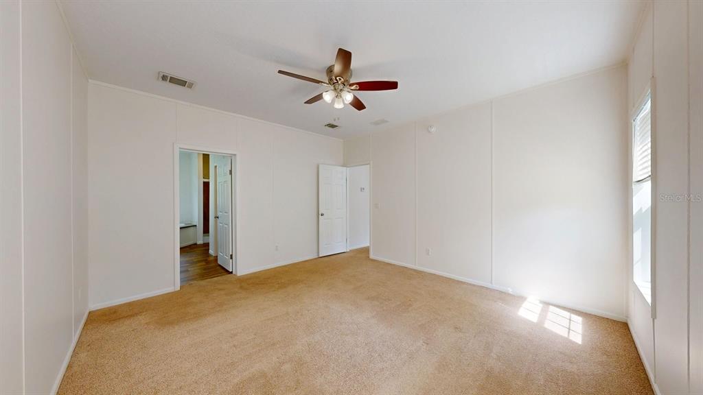 A bedroom with beige carpet, white paneled walls, a ceiling fan, and two doorways — 2930 PALMETTO STREET, BUNNELL, FL