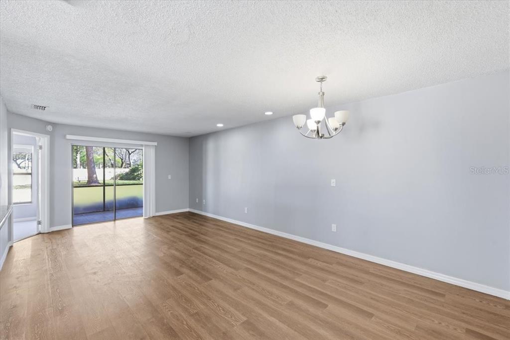 A spacious living area features light gray walls, wood-look flooring, and a sliding glass door — 7813 SUGAR BROOK COURT UNIT 7813, ORLANDO, FL