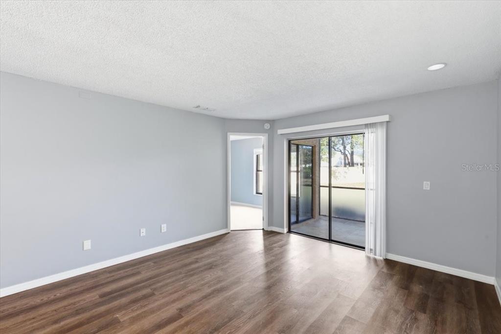 An empty room with light gray walls, dark wood-look flooring, and a sliding glass door — 7813 SUGAR BROOK COURT UNIT 7813, ORLANDO, FL